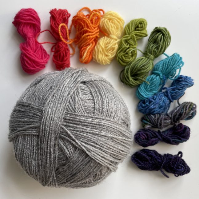 A grey ball of yarn and butterflies of yarn in rainbow colours.